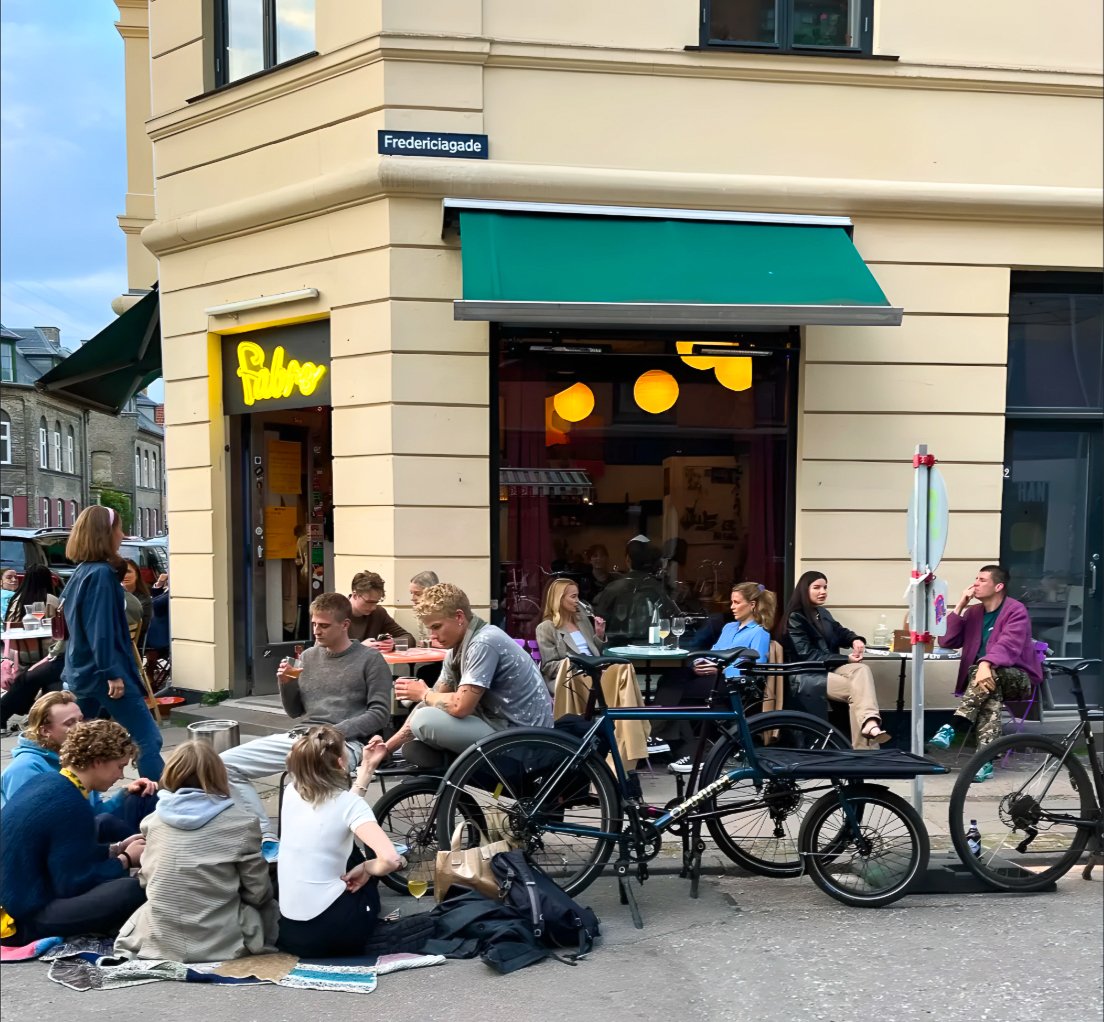 Fabro's corner restaurant in Copenhagen with a green awning, the yellow Fabro sign and guests eating outside