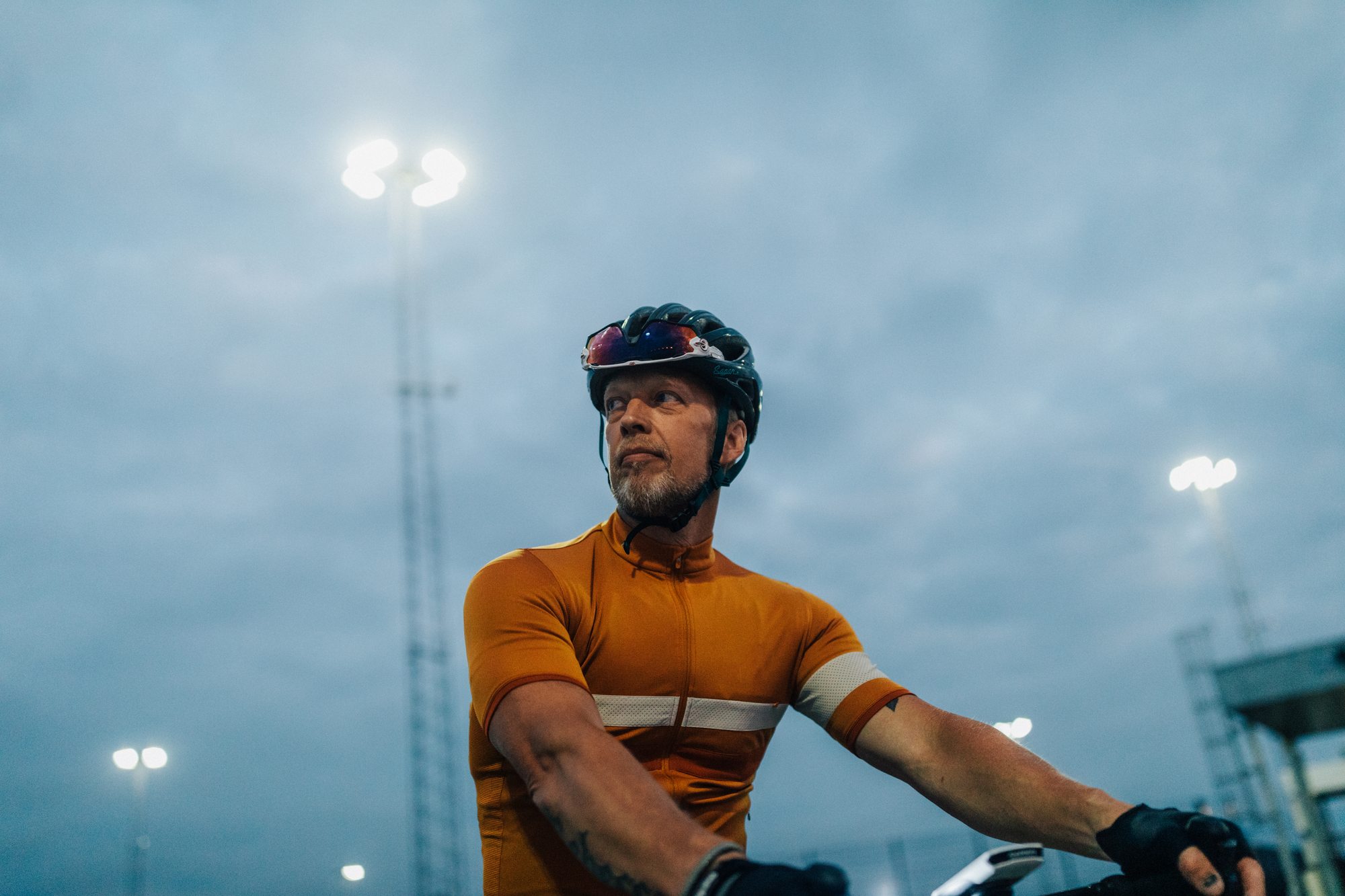 A man in cycling gear under floodlights at dusk
