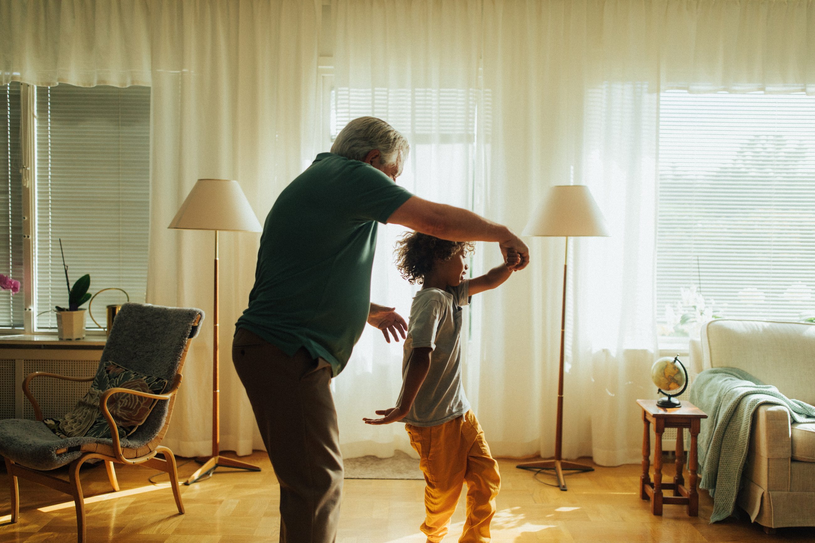 A grandfather dancing with his grandchild in a sunlit living room