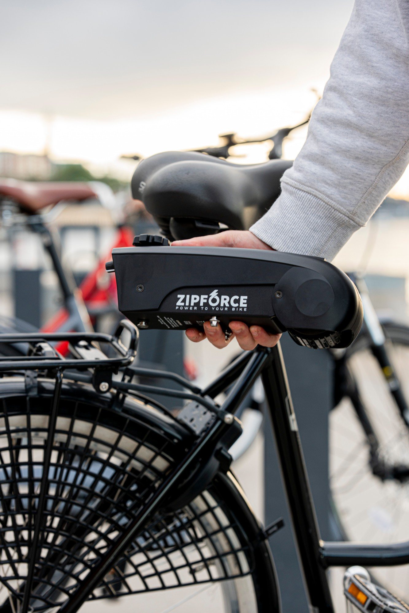 A hand lifting the Zipforce motor onto a black bike at a rack